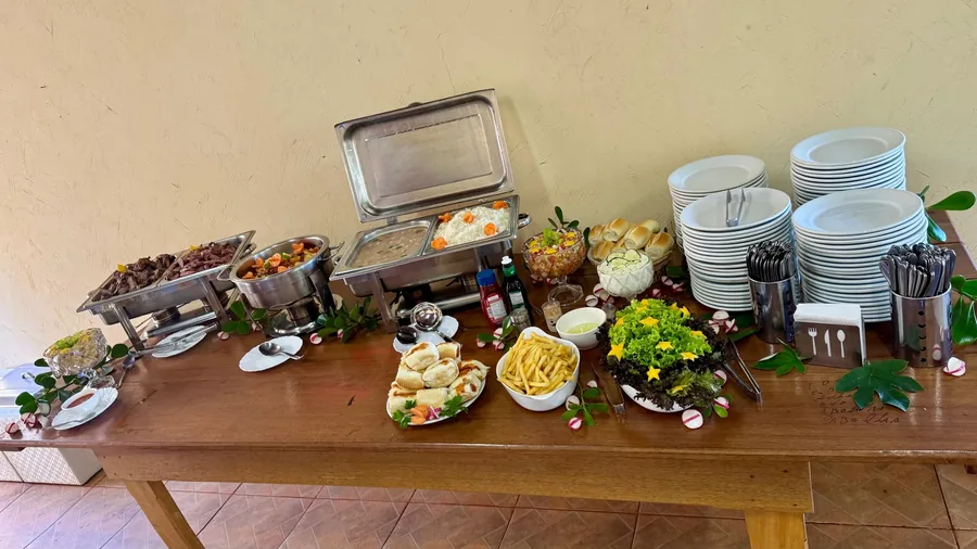 Buffet organizado com pratos empilhados, talheres e acompanhamentos variados