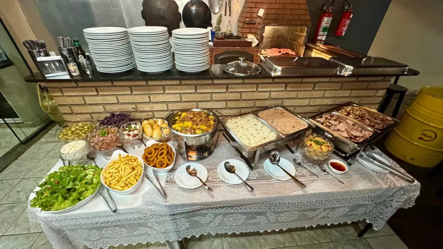 Mesa de churrasco junto à churrasqueira, com pratos e talheres organizados